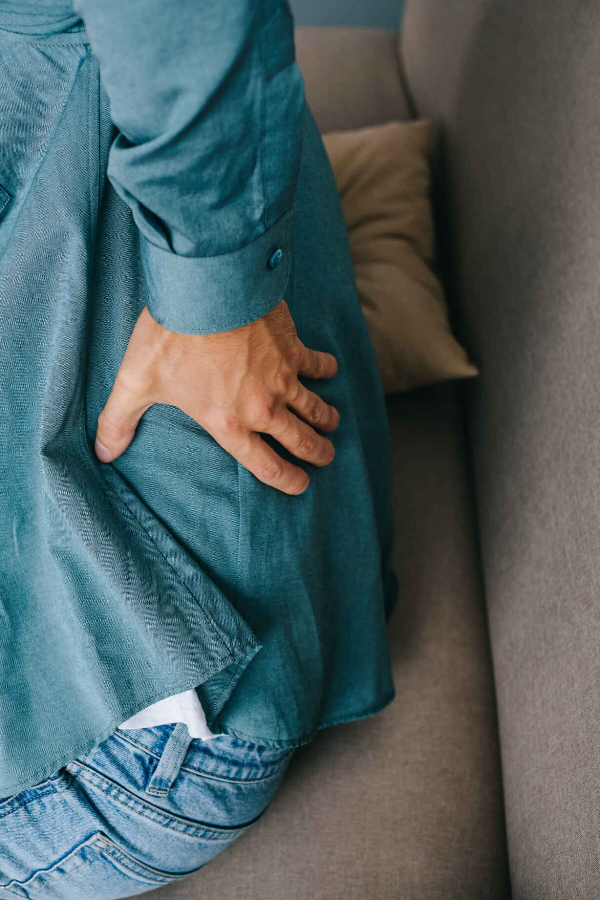 cropped shot of man sitting on sofa and suffering from back pain
